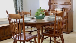 Una mesa de comedor de madera rodeada por seis sillas, una planta verde en una maceta blanca y un aparador de madera con platos.