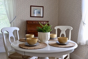 A dining table with four bowls and a potted plant, surrounded by white chairs.