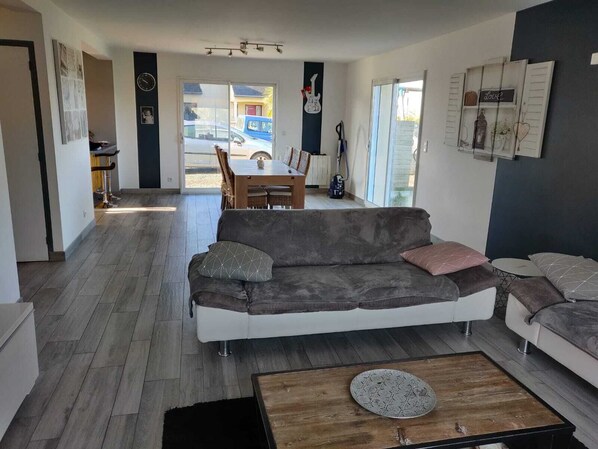 Un salon moderne avec un canapé gris, une table basse et un coin repas comprenant une table et des chaises.