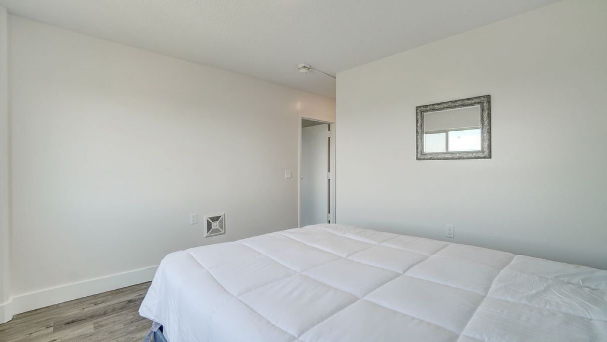 A bedroom with a bed, a door, and a wall-mounted mirror.