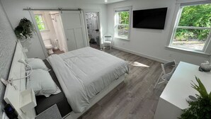 A modern bedroom with a large bed, a desk, and a TV.