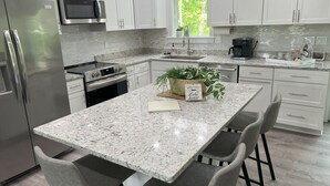A modern kitchen with white cabinets, stainless steel appliances, a granite countertop, and a central island with bar stools.