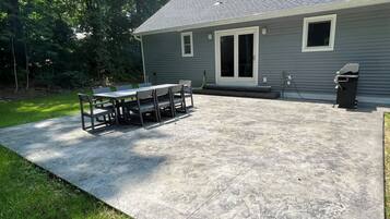 A concrete patio with a table and chairs, a covered area, and a house with a gray exterior and a garage door.