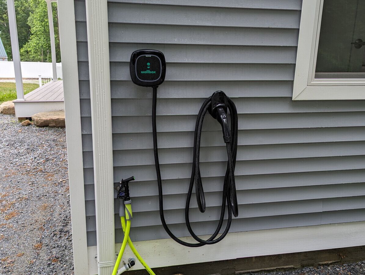 Une borne de recharge pour véhicules électriques fixée au mur, avec un câble relié à un véhicule.