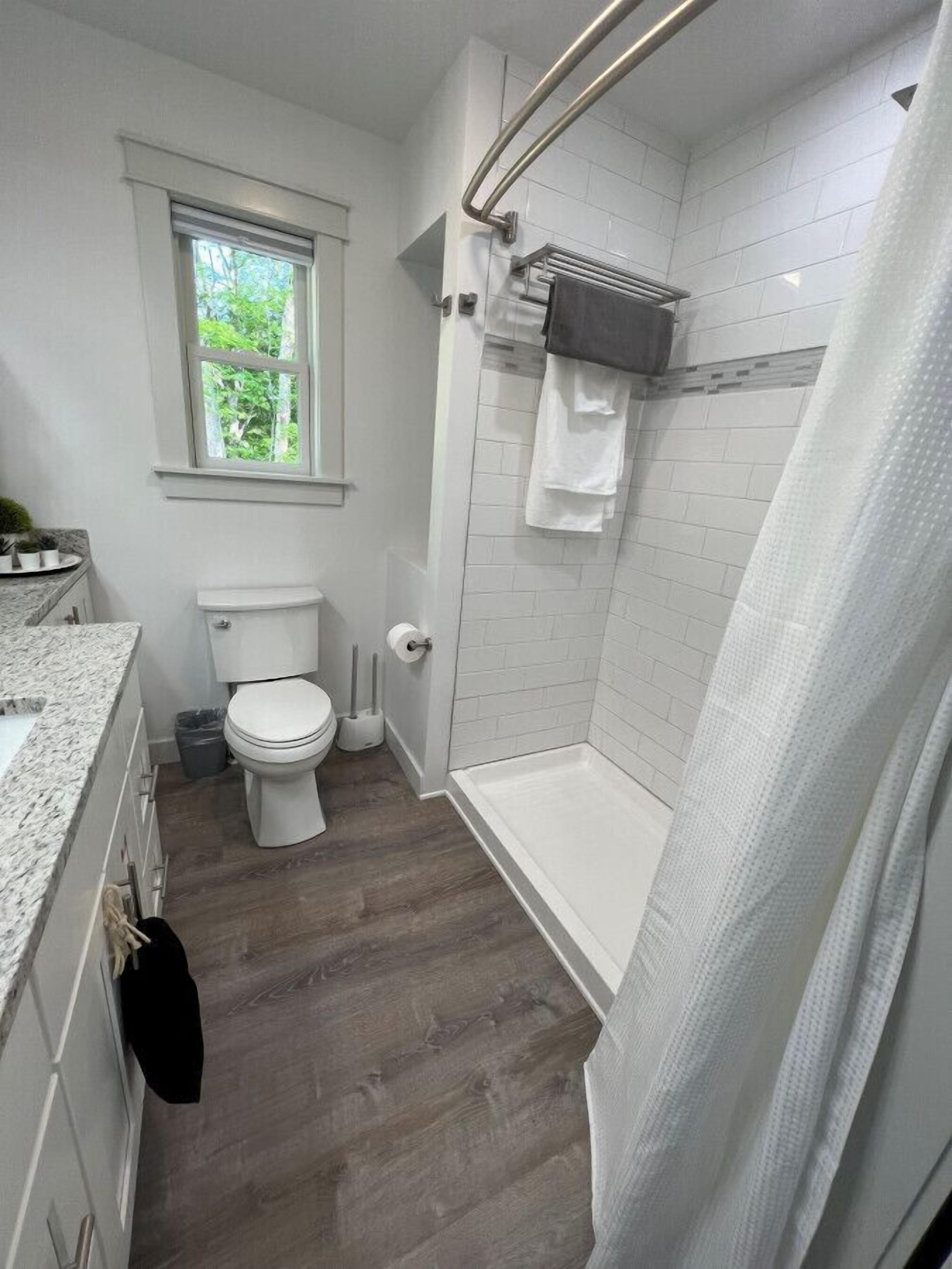 A bathroom with a toilet, shower, and a window.