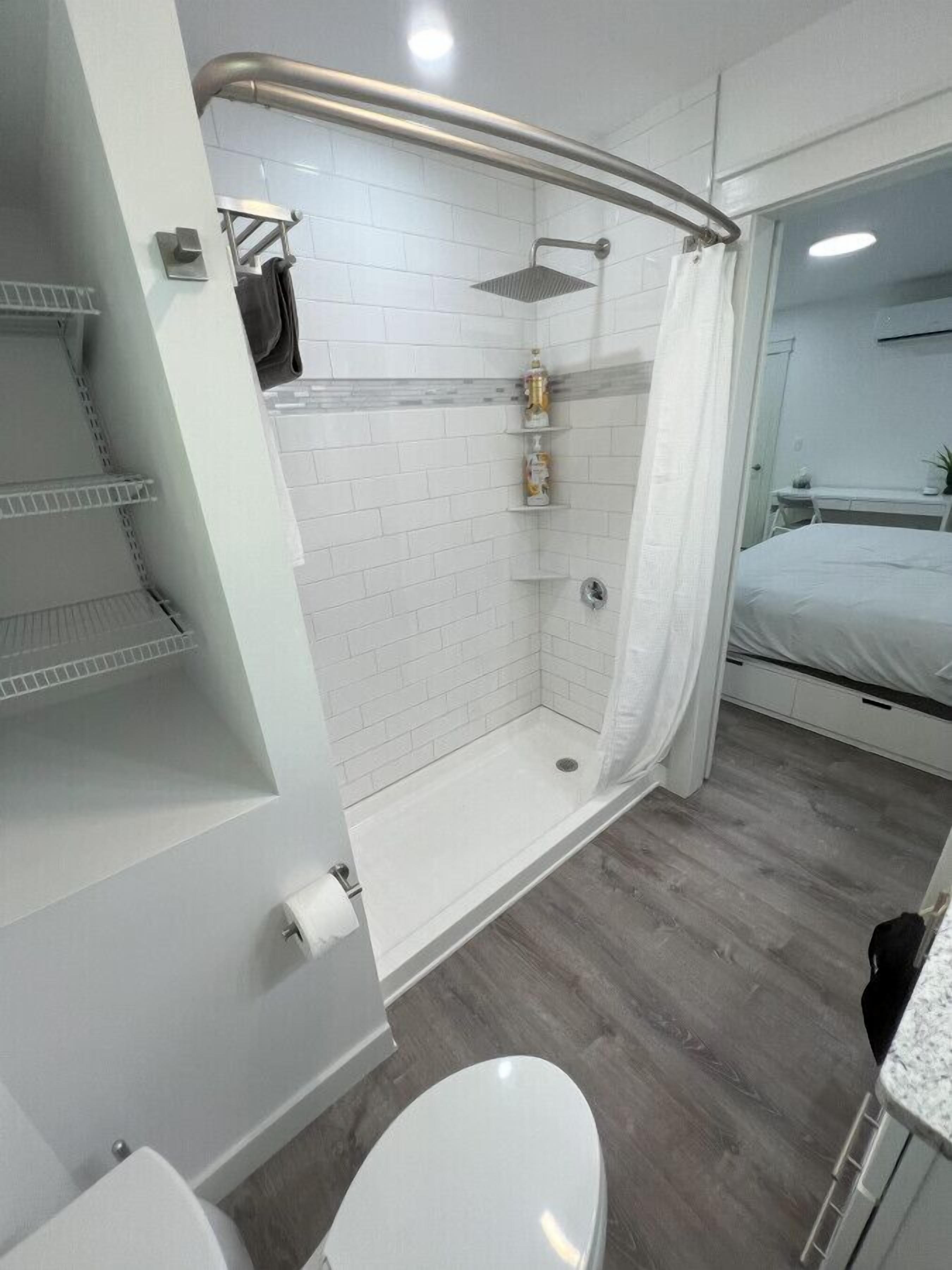 Un baño moderno con cabina de ducha de vidrio, paredes de azulejos blancos y suelo de madera.