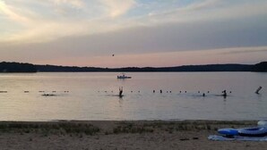 A beach with a calm sea, a boat, and some people in the water.