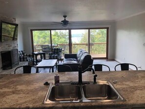 A kitchen with a double sink, a dining area with a table and chairs, a fireplace, and a balcony with a view of trees. - Great retreat! Close to lake and marina (Mountain Home)