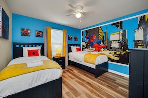 Une chambre avec deux lits, un ventilateur de plafond et une grande fresque représentant Spider-Man sur le mur.