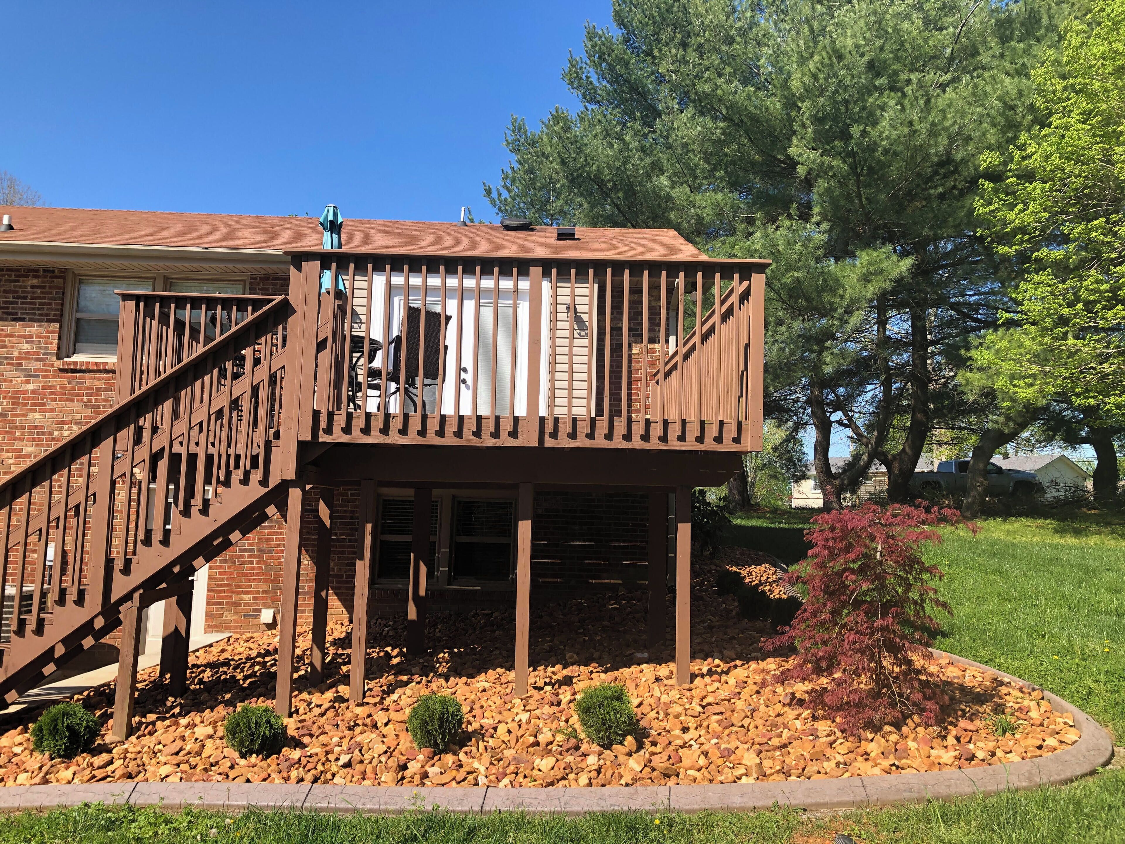 A two-story deck with a staircase, surrounded by a landscaped garden with rocks and small shrubs.