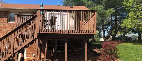 A two-story deck with a staircase, surrounded by a landscaped garden with rocks and small shrubs.