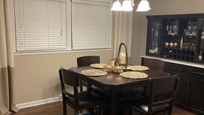 A dining area with a dark wooden table, four chairs, a chandelier, and a kitchen area with a dark cabinet and various kitchen items. - Home away from home 37043 (Clarksville)