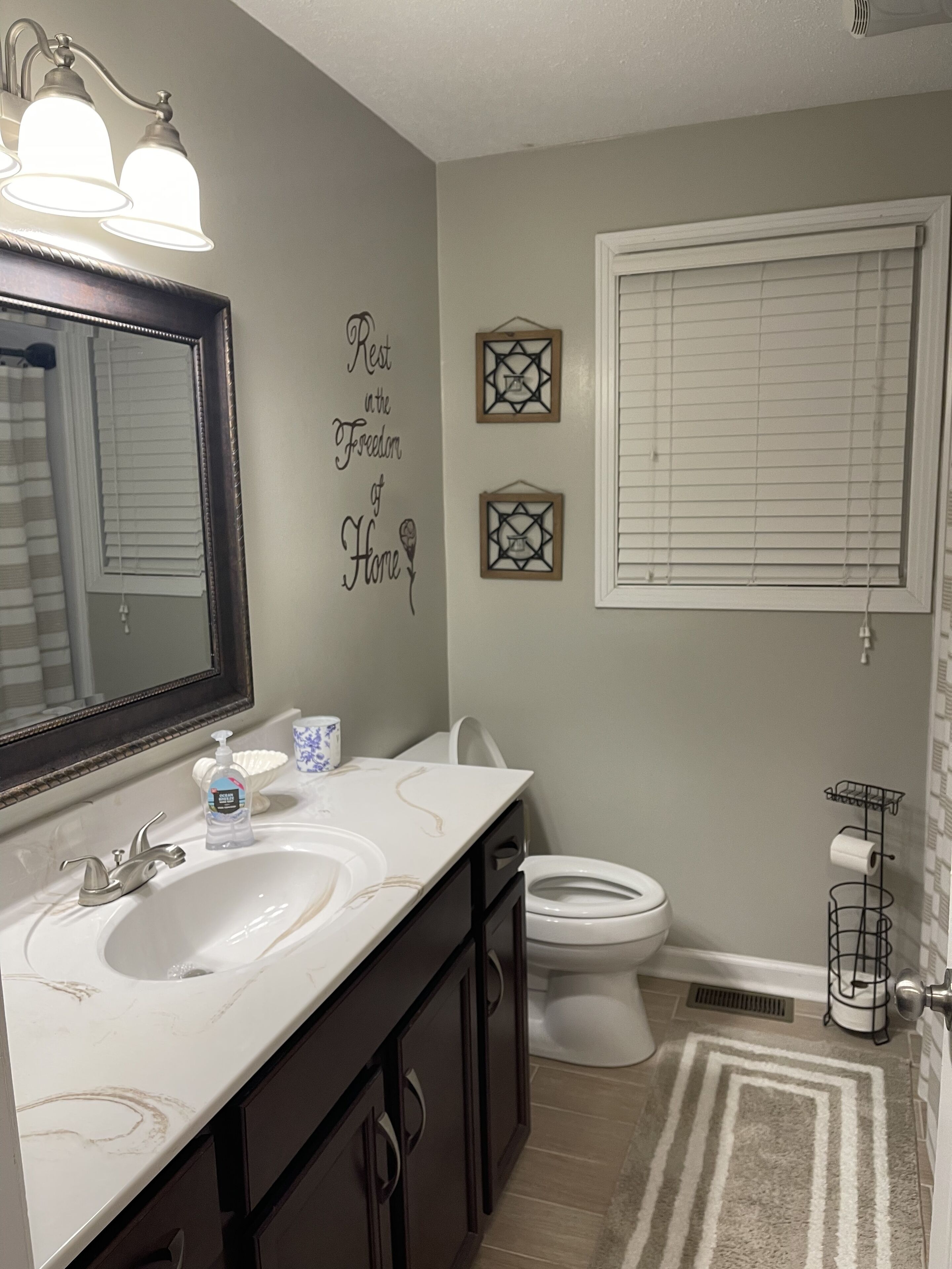 A bathroom with a double sink, a toilet, a mirror, and decorative wall art.