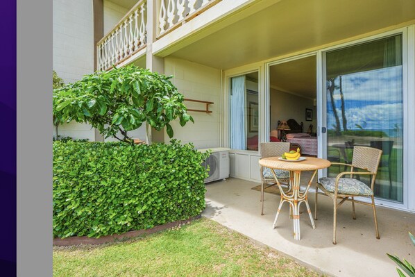 Un balcon avec une table et des chaises pour prendre les repas, un petit arbre et une vue sur l’océan, visible à travers une porte vitrée.