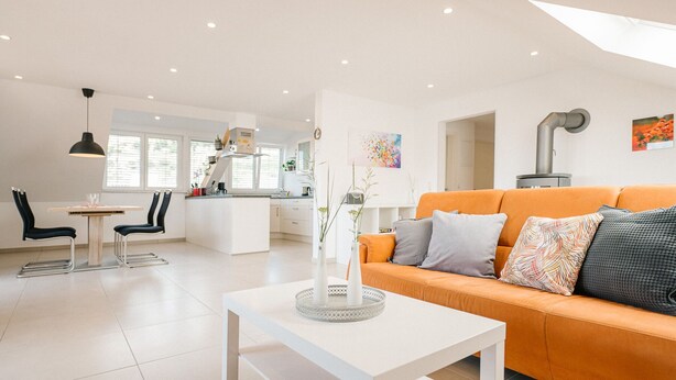 Una sala de estar moderna con un sofá blanco, una mesita pequeña blanca y una cocina al fondo.