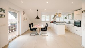 Una cocina moderna con armarios blancos, una isla central y un comedor con mesa y sillas.