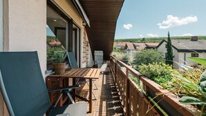 Un balcón de madera con una mesa y sillas, con vistas a una zona residencial con casas y vegetación.