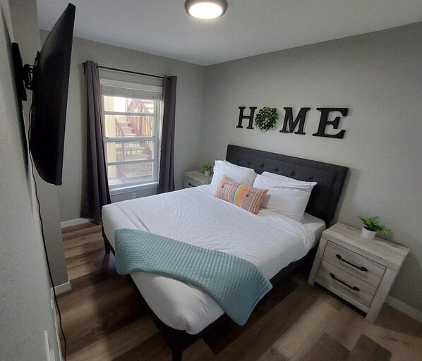 A bedroom with a bed, a nightstand, a TV mounted on the wall, and a window with curtains. - Amazing 3/2 Condo, gated community at Club Cortile!! (Kissimmee)