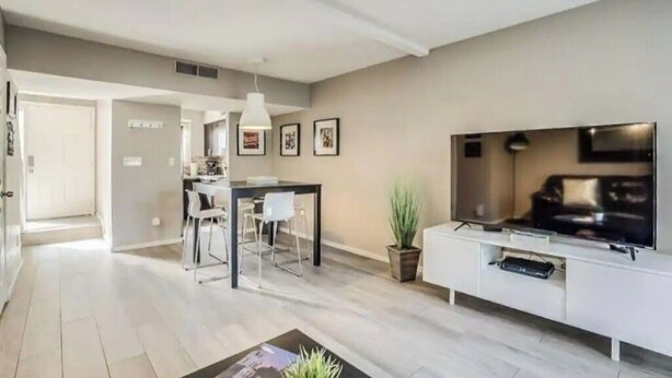 Ein modernes Wohnzimmer mit Flachbildfernseher, einem Essbereich mit Tisch und Stühlen sowie einer Küche im Hintergrund.