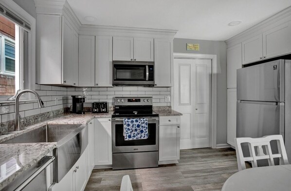 A kitchen with white cabinets, a stainless steel refrigerator, a microwave, a stove, and a sink.