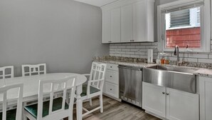 Una cocina con armarios blancos, un lavamanos de acero inoxidable y una ventana con persianas.