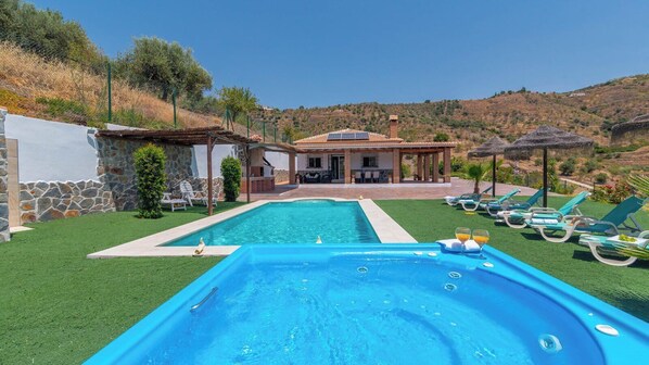 A swimming pool with lounge chairs, a stone wall, and a house with a tiled roof. - Casa La Fuente Pinta Arenas by Ruralidays (Málaga)