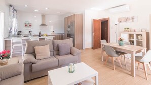 Un salon moderne avec un canapé, une table à manger et un coin cuisine à l’arrière-plan.