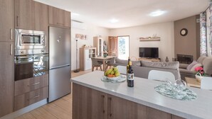 Une cuisine moderne dotée d’appareils électroménagers intégrés, un coin repas avec une table et des chaises, et un salon avec un canapé et une télévision.