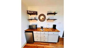 A kitchen with a wooden countertop, a microwave, a coffee maker, and a sink. There are two white cabinets and a white refrigerator. - New Encanto Suites with Private Hot Tub | Secluded (Fredericksburg)