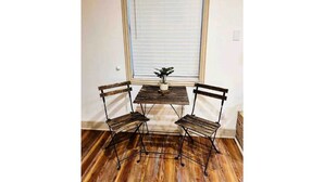 A corner room with a wooden floor, a small table with two chairs, and a window with blinds. - New Encanto Suites with Private Hot Tub | Secluded (Fredericksburg)