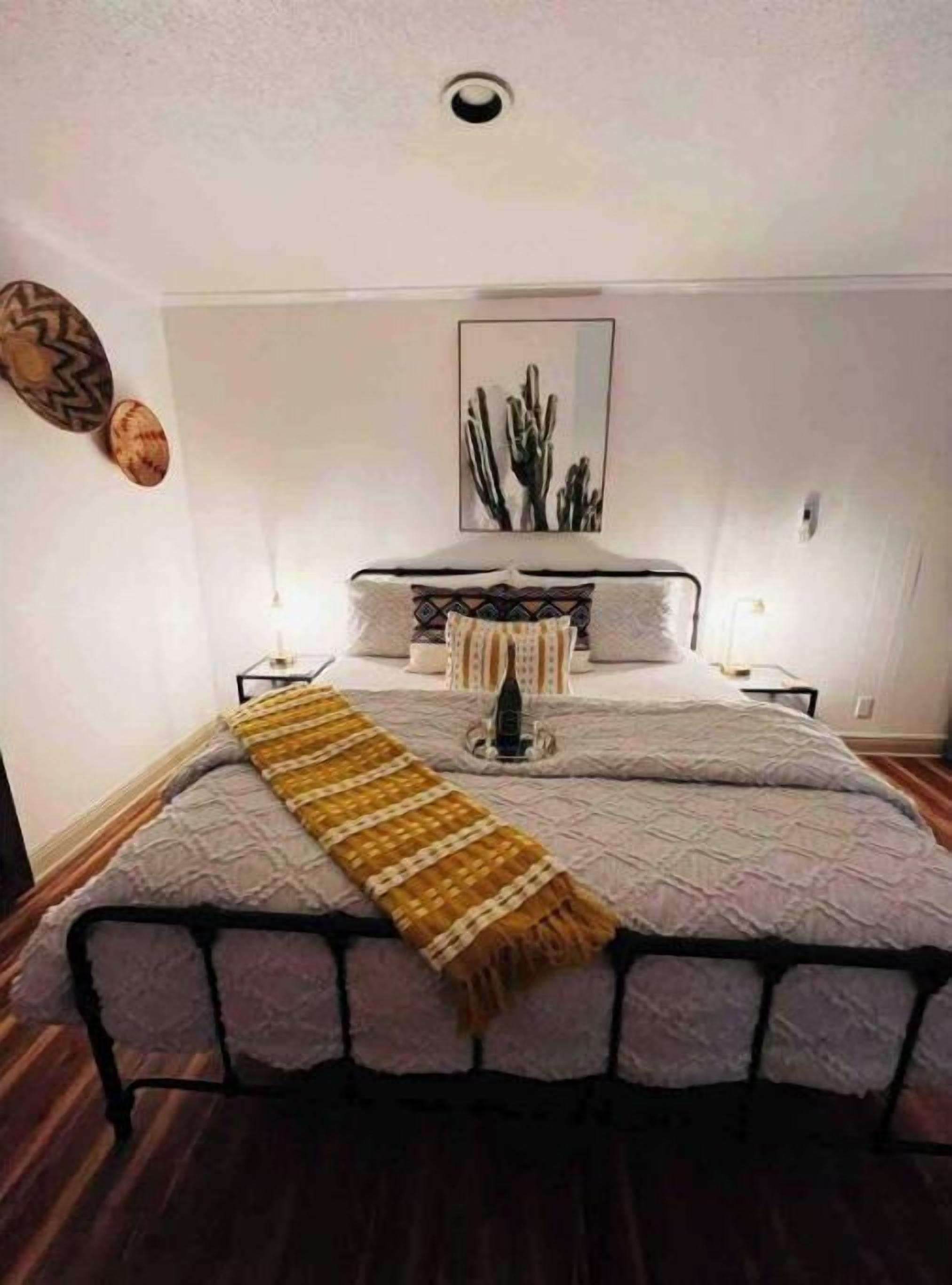 A bedroom with a bed, a bedside table, a nightstand, a wall-mounted artwork, and a wooden floor.