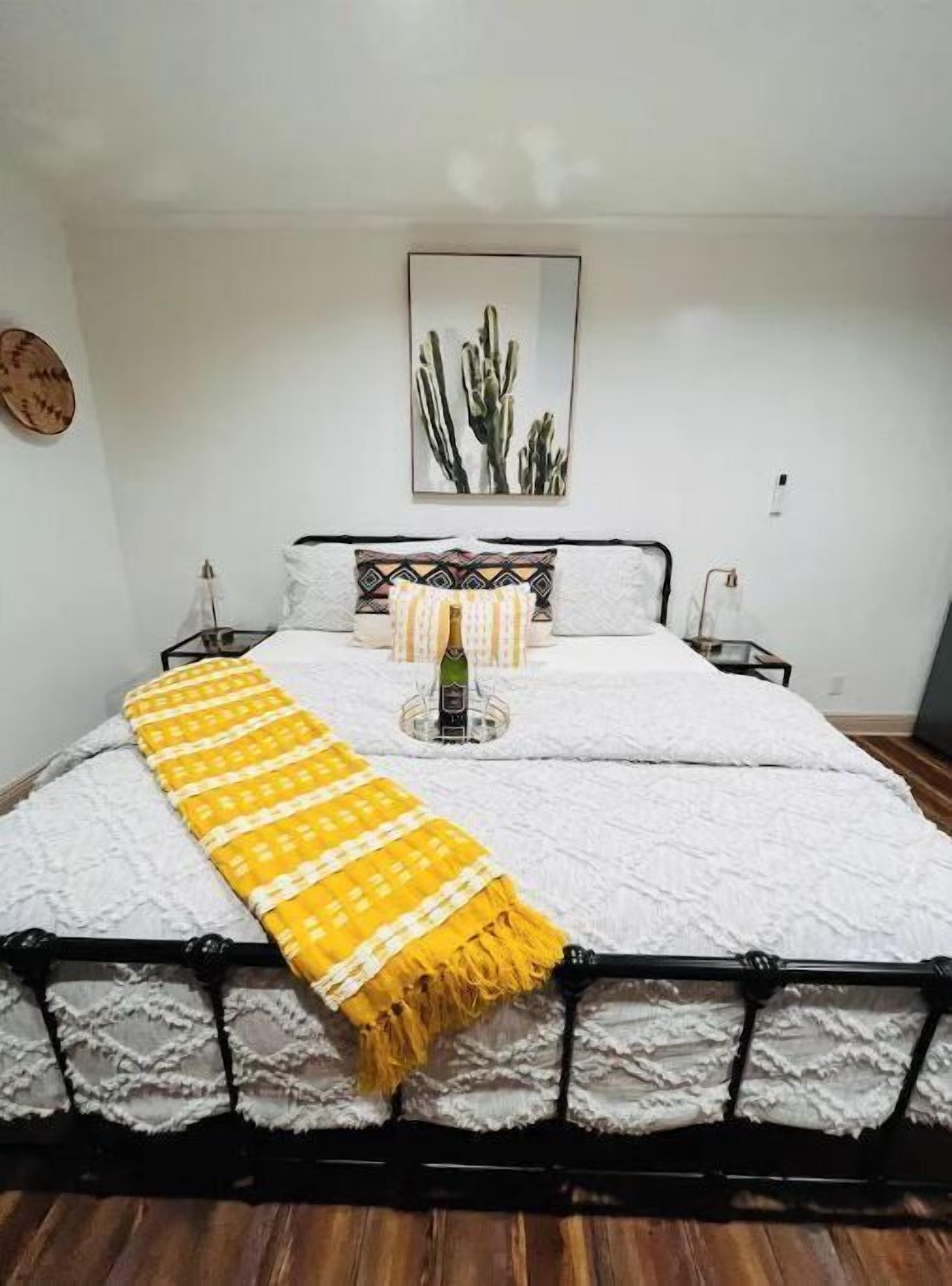 Una cama con un edredón blanco, una manta amarilla y una obra de arte con un cactus encima.
