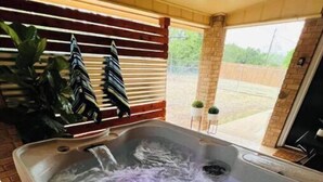 A hot tub with water bubbling, surrounded by a brick patio and a wooden fence. - New Encanto Suites with Private Hot Tub | Secluded (Fredericksburg)