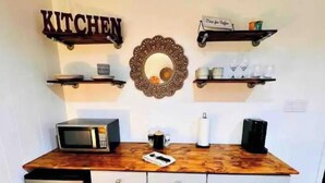 Une cuisine dotée d’un plan de travail en bois, d’un four à micro-ondes, d’une machine à café et d’un évier. On y trouve deux armoires blanches et un réfrigérateur blanc.