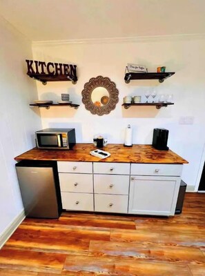 A kitchen with a wooden countertop, a microwave, a coffee maker, and a sink. There are two white cabinets and a white refrigerator.