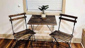 Une pièce d’angle avec un plancher en bois, une petite table avec deux chaises et une fenêtre avec des stores.
