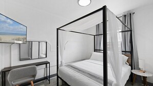 A modern bedroom with a four-poster bed, a bedside table, a chair, and a large mirror. - Shorehaven 2- Updated and Stylish 2 bedroom 14 St! (Ocean City)