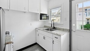 A small kitchen with white cabinets, a granite countertop, a sink, and a window. - Shorehaven 2- Updated and Stylish 2 bedroom 14 St! (Ocean City)
