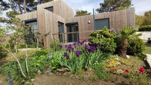 A modern house with a wooden exterior, surrounded by a garden with various plants and flowers. - Air-conditioned mini-house near the beaches, built in 2022 (Pornichet)