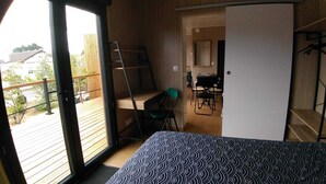 A room with a bed, a desk, and a chair. There is a door leading to an outdoor area with a wooden deck. - Air-conditioned mini-house near the beaches, built in 2022 (Pornichet)