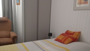 Sängyssä on raidallinen päiväpeite, huoneessa on tuoli, vaatekaappi ja seinällä kehystetty kuva.