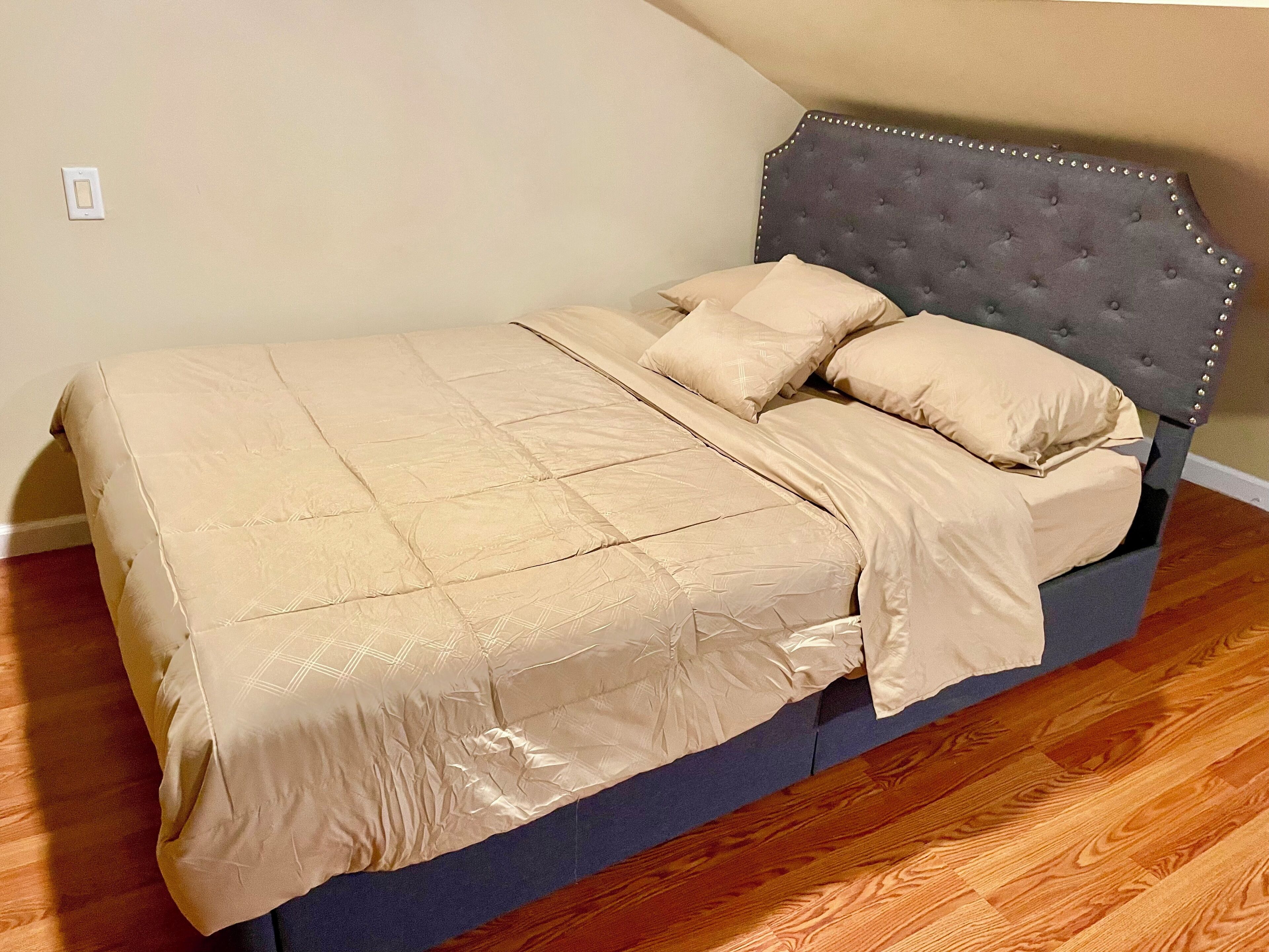 A bed with a tufted headboard, a beige quilt, and matching pillows.