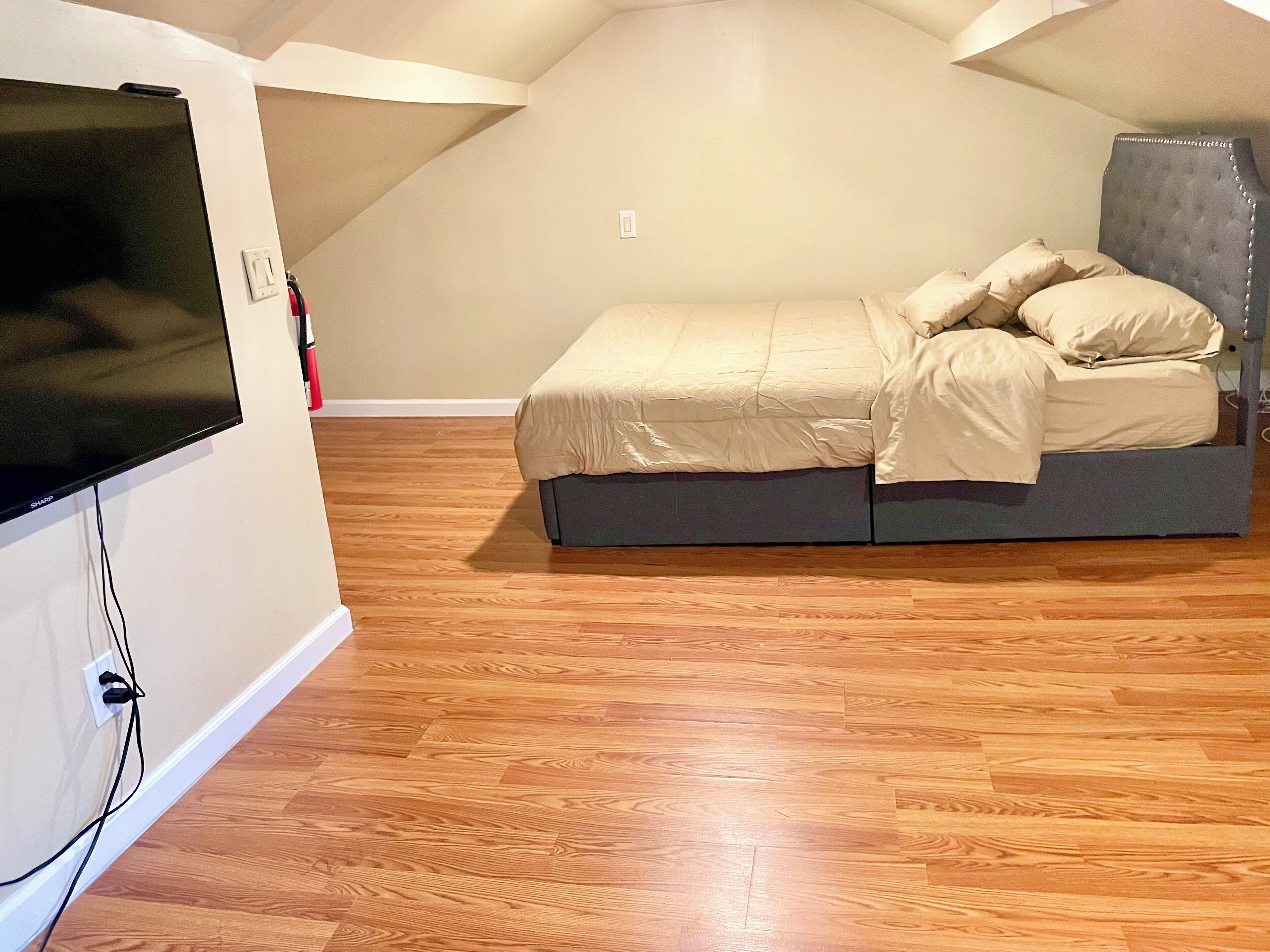 A bedroom with a bed, wooden flooring, and a television mounted on the wall.