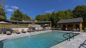 Ein Pool mit Liegestühlen und einer überdachten Liegefläche, umgeben von einem Zaun und Bäumen.