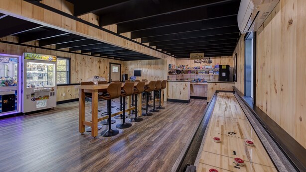 A wooden interior with a shuffleboard table, bar stools, and a vending machine.
