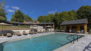 A swimming pool with lounge chairs and a covered area, surrounded by a fence and trees.