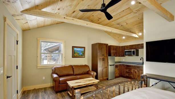Una habitación acogedora con techo de madera, un sofá de cuero marrón, una mesita de centro de madera y una cama.