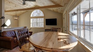 Une pièce chaleureuse avec un plafond en bois, une grande fenêtre en arc de cercle, une table ronde en bois et un canapé en cuir.