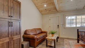 Una habitación con un sofá de cuero marrón, una mesa de madera con una planta, una silla de madera y un mueble de madera grande.