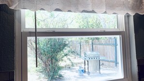 Una ventana con un frente blanco y vistas a un patio trasero con una parrilla y plantas.